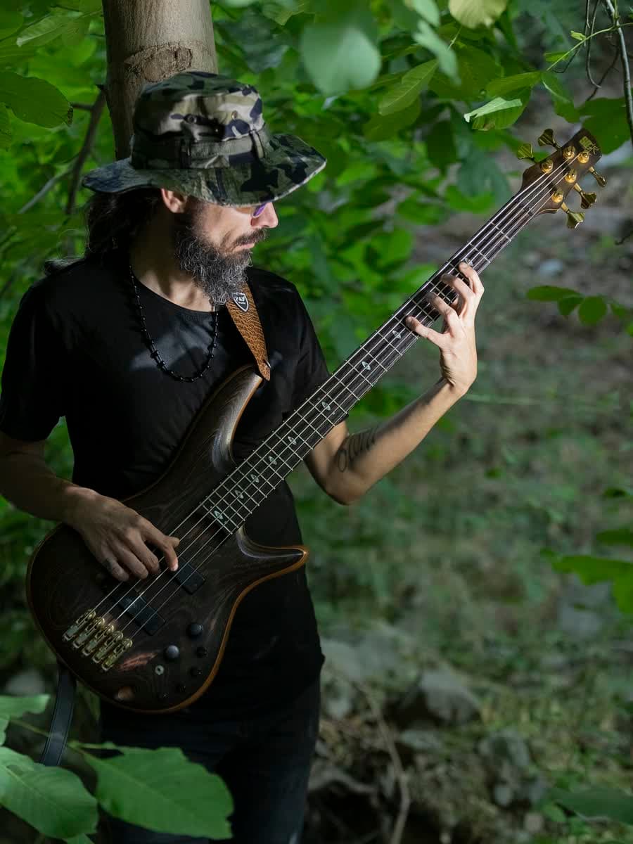 Baixista tocando: mão esquerda trasteando o braço, mão direita atacando as cordas, alça apoiando o instrumento.
