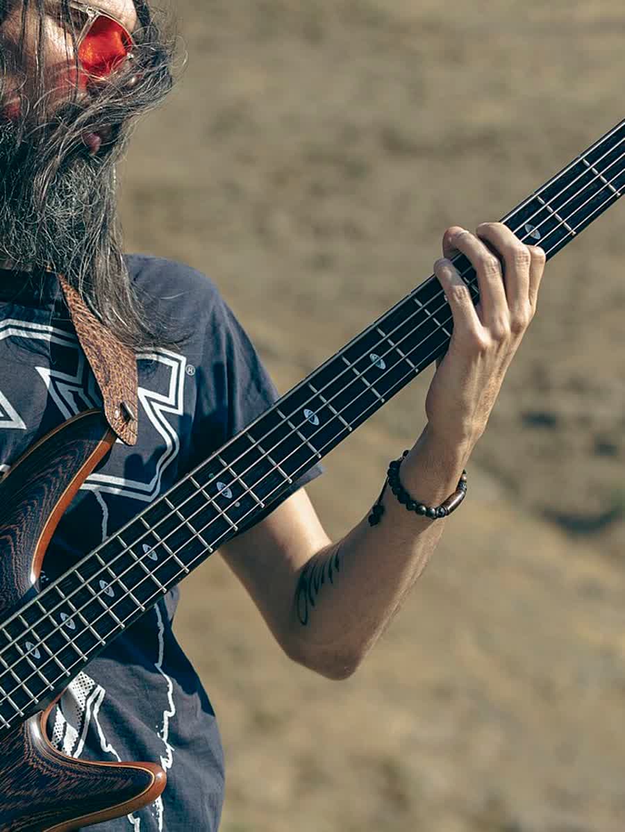 Baixista tocando, mãos no braço, num campo aberto.