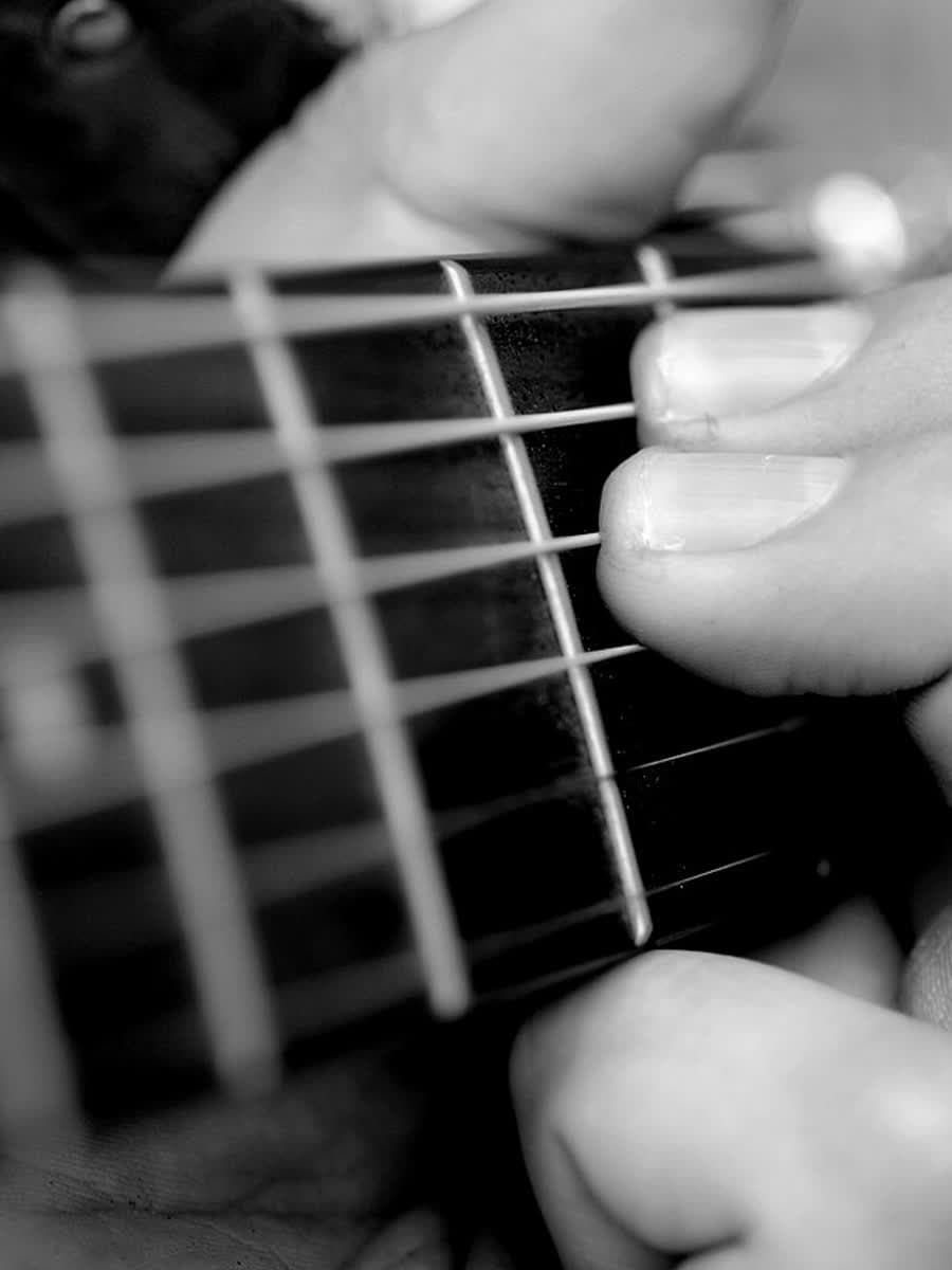 Mão esquerda pressionando um acorde no braço do violão.